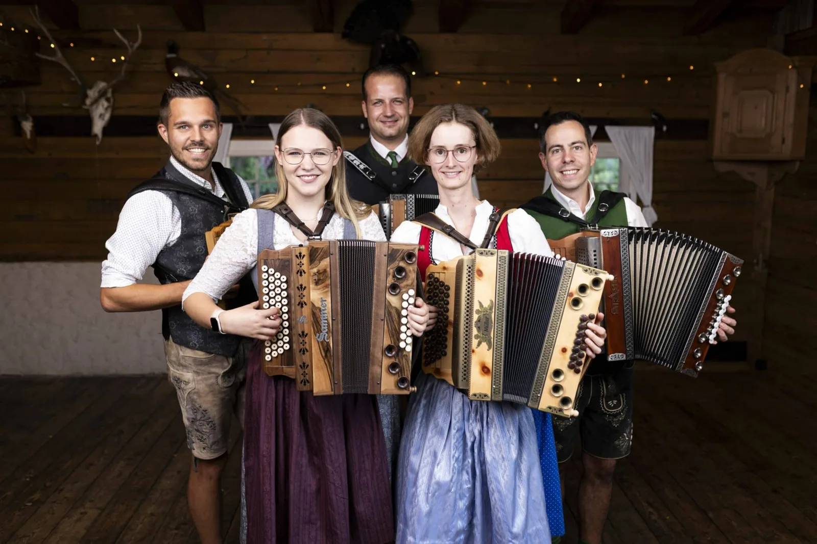 Fünf Personen mit Steirischen Harmonikas in Tracht vor Holzbalkendecke