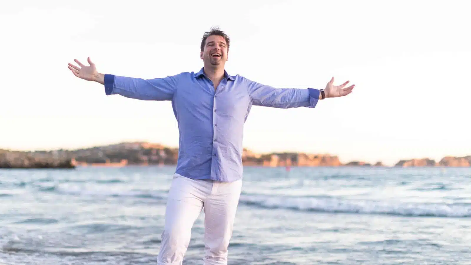Björn Heede mit ausgebreiteten Armen am Strand bei Sonnenuntergang