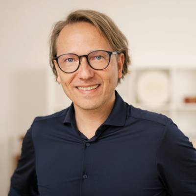 Porträt von Nikolaus Lackner, Mann mit braunem Haar, Brille, dunklem Hemd