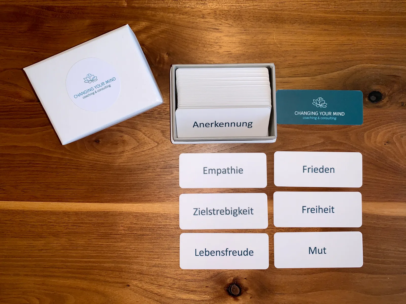 Coaching-Kartenset mit Wertekarten auf Holztisch: Empathie, Frieden, Zielstrebigkeit, Freiheit, Lebensfreude, Mut neben Verpa