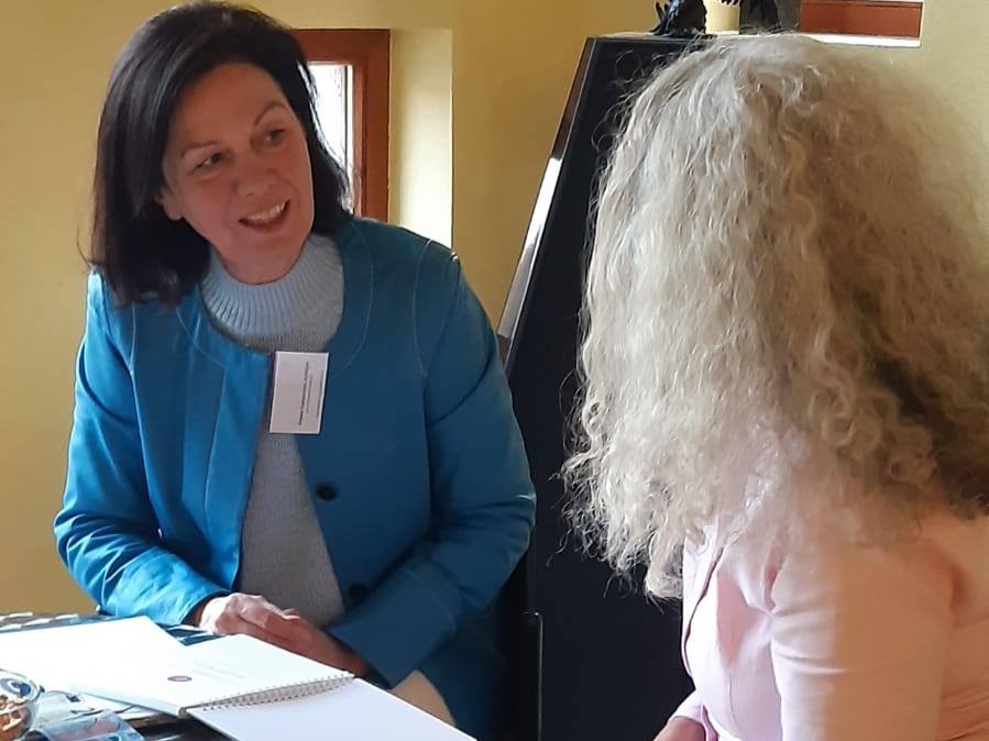 Susanne G. im Gespräch mit einer Coachin in Büroumgebung, sitzend an einem Tisch mit Unterlagen