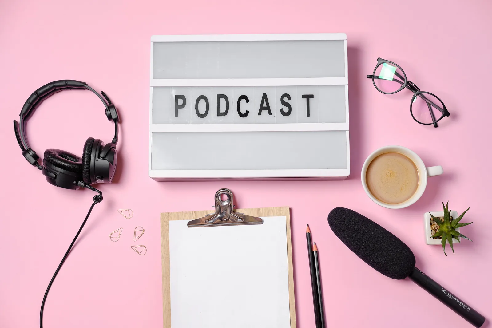Podcast-Leuchtkasten mit Kopfhörer, Brille und Kaffeetasse auf rosa Untergrund