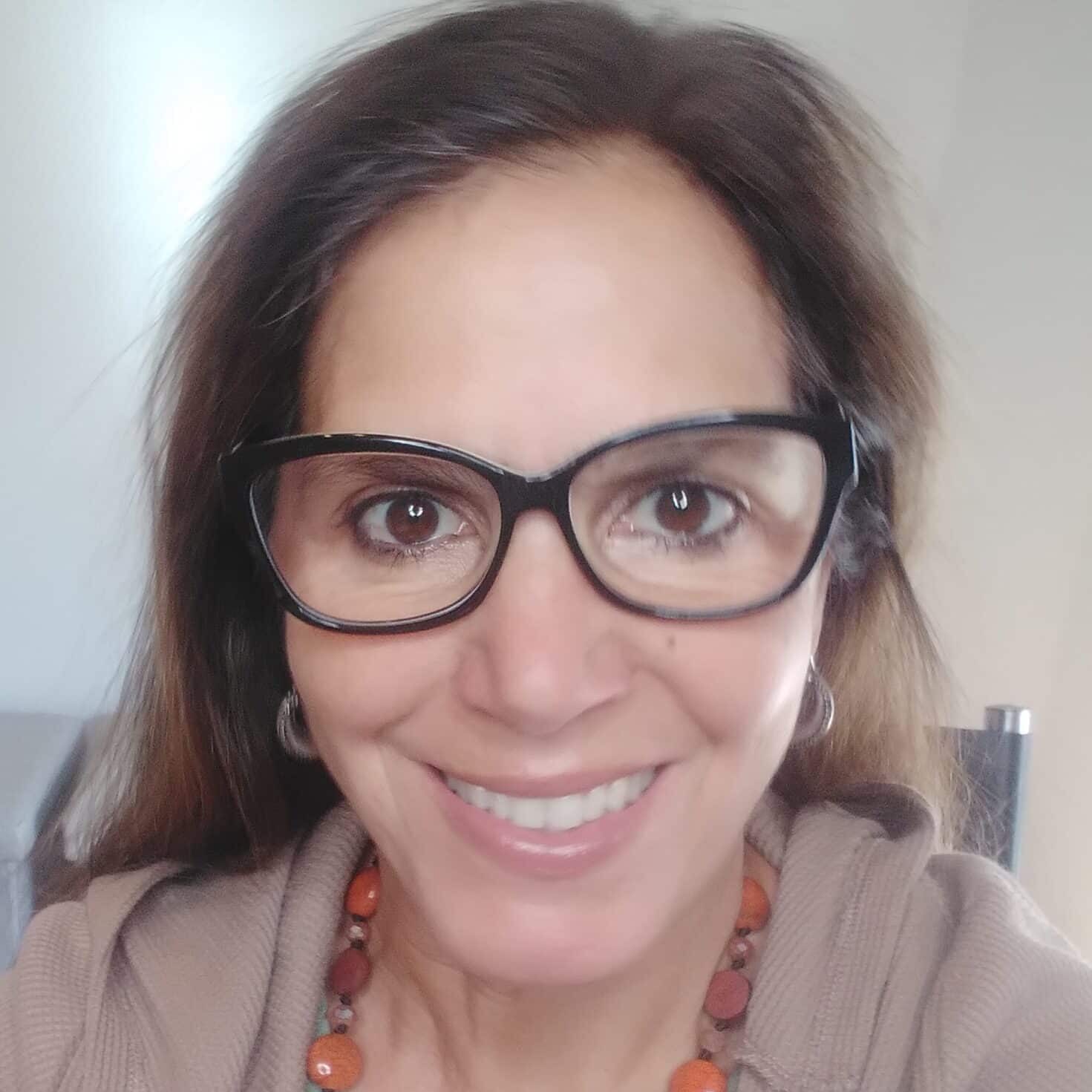 Porträt Alessandra Fois mit Brille und Perlenkette vor hellem Hintergrund