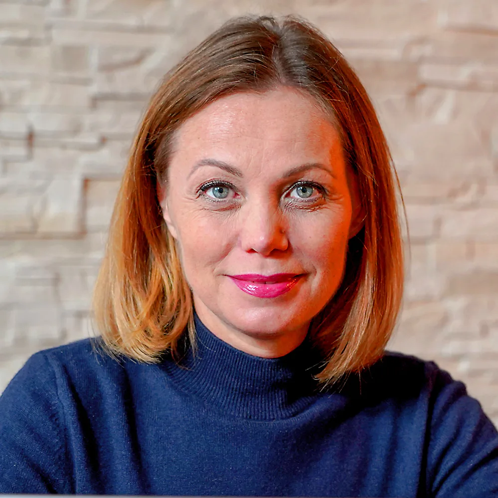 Christiana Schweizer Porträt mit rötlichem Haar, dunkler Rollkragenpullover, vor Ziegelmauer, direkt in Kamera blickend