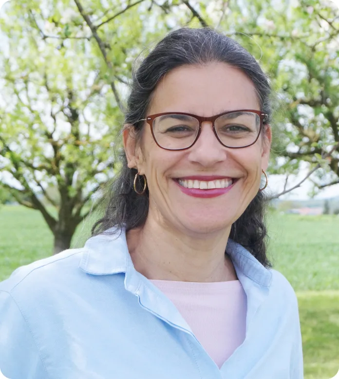 Porträt einer Frau mit Brille und Lächeln vor grünem Baum-Hintergrund