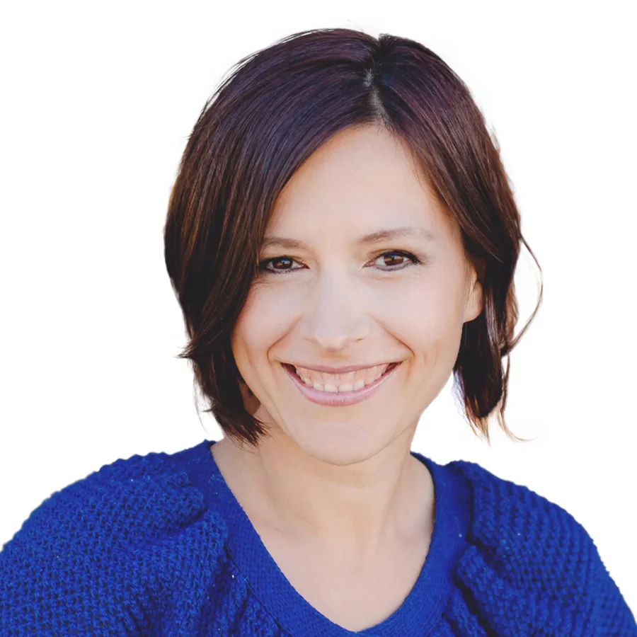 Porträtfoto von Katrin Klug, Frau mit braunen Haaren, blauem Pullover, lächelnd vor weißem Hintergrund