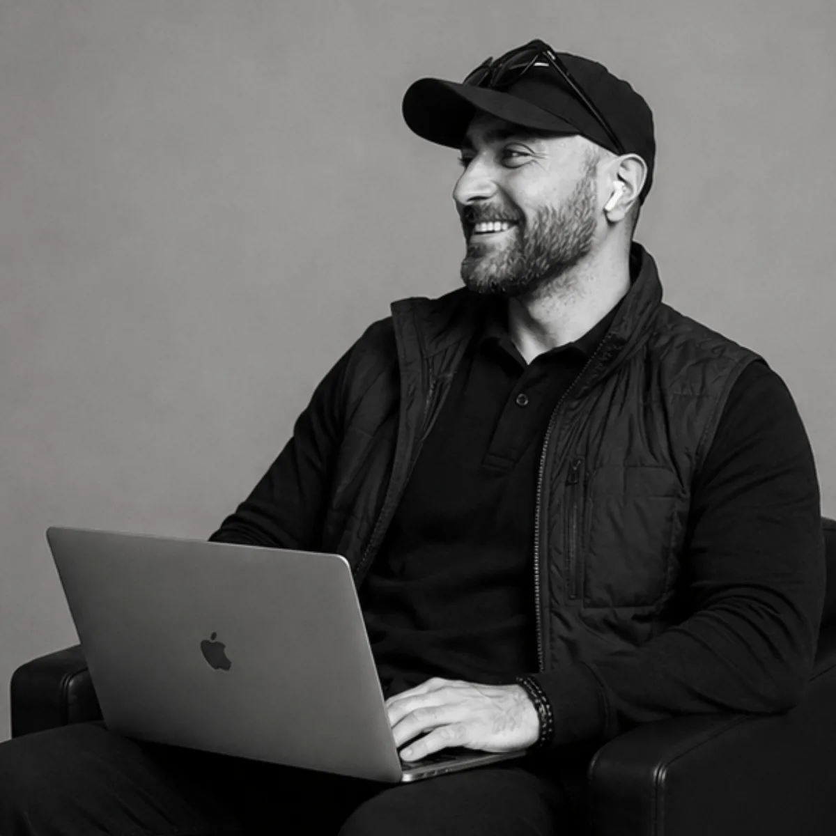 Schwarz-Weiß-Porträt von Kadir Demir mit Basecap, schwarzer Jacke und Laptop