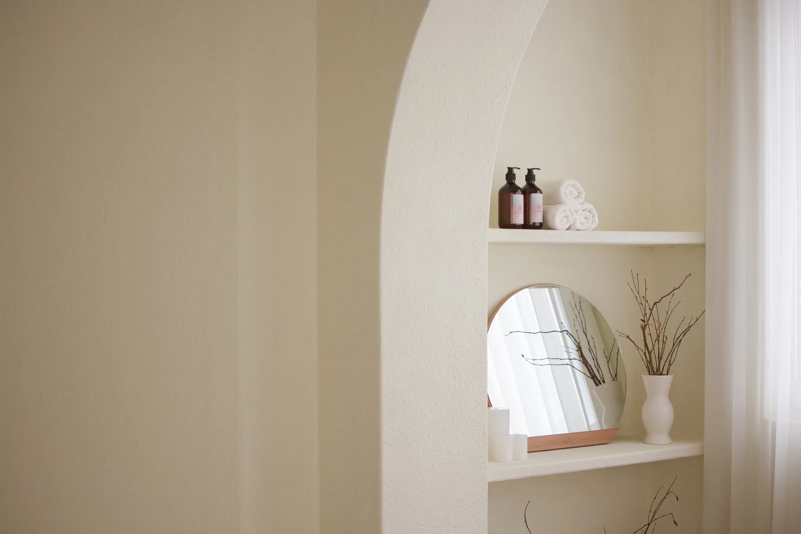 Minimalistische Badezimmer-Nische mit weißen Regalen, Spiegeln und Wellness-Produkten