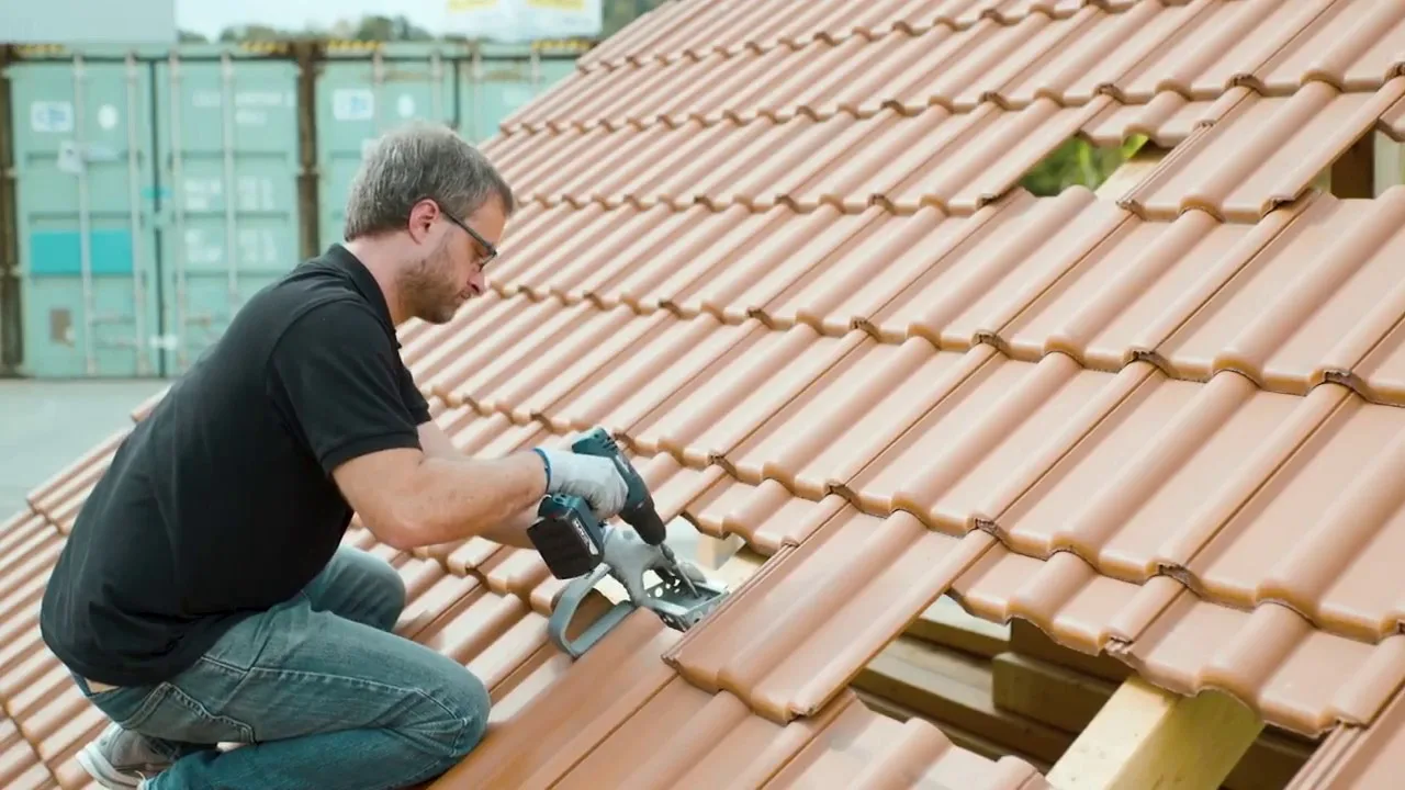 Fertig gedecktes Dach mit terracotta-farbenen Ziegeln, Dachrinnen und Fallrohren bei Tageslicht