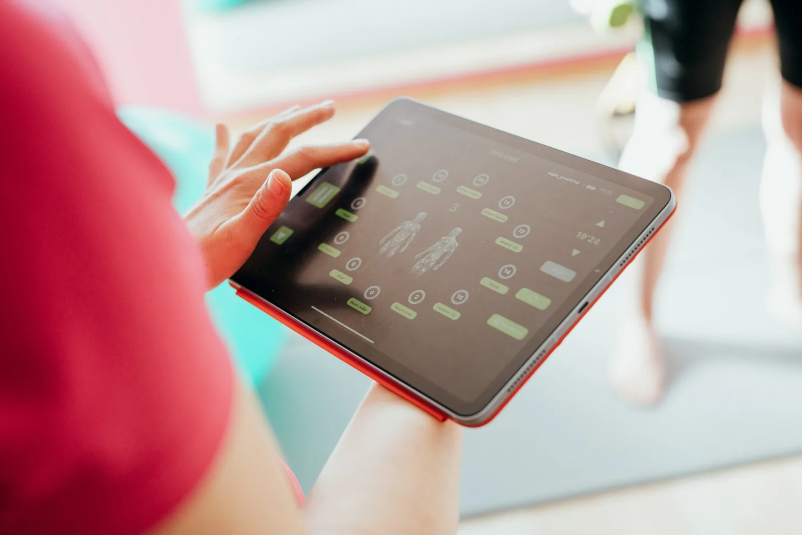 Frau in rosa Shirt bedient Tablet mit Rückenanalysesoftware und Körpergrafiken