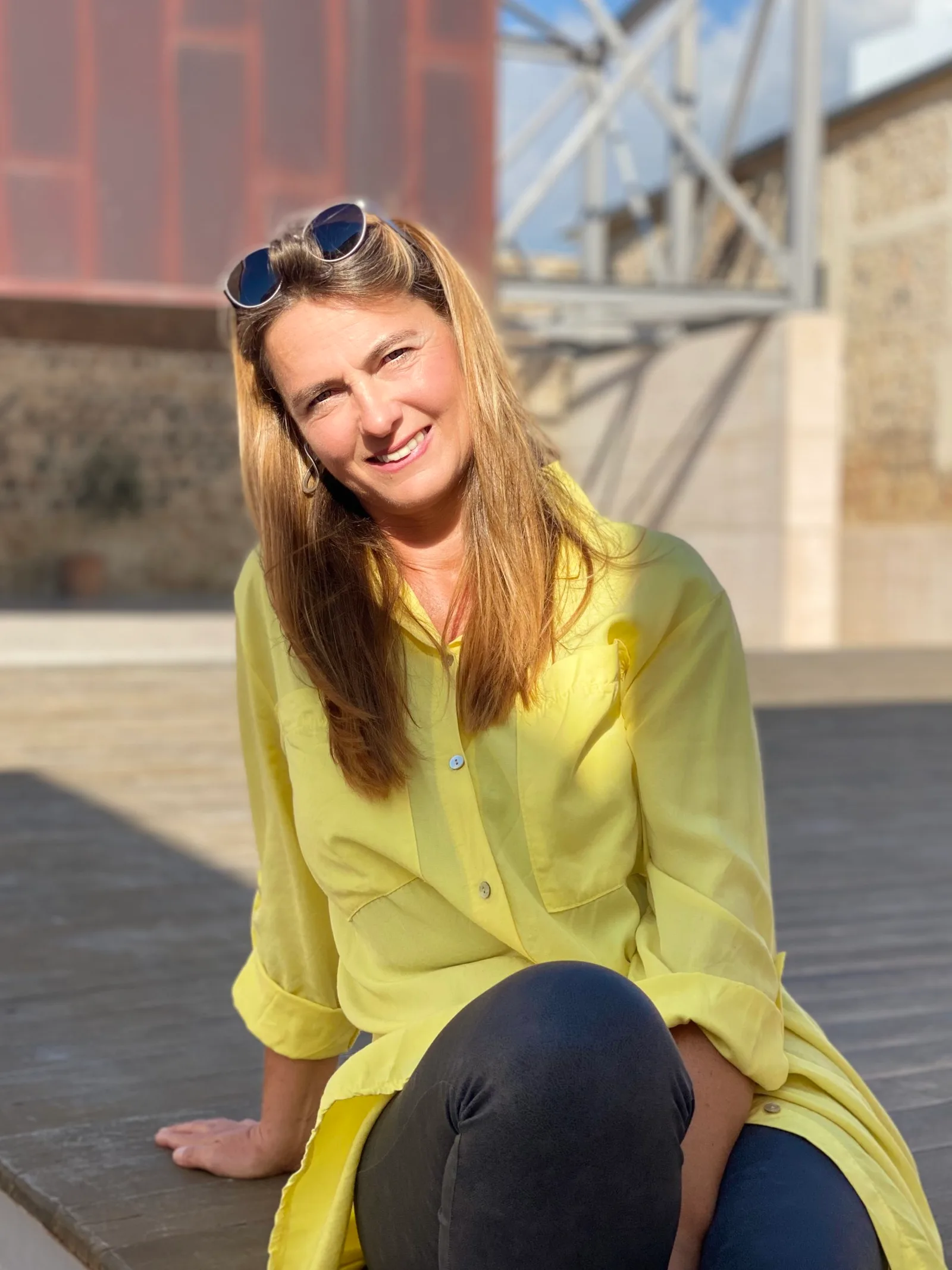Frau in gelber Bluse auf Dachterrasse mit Stadtkulisse, lächelt in die Kamera