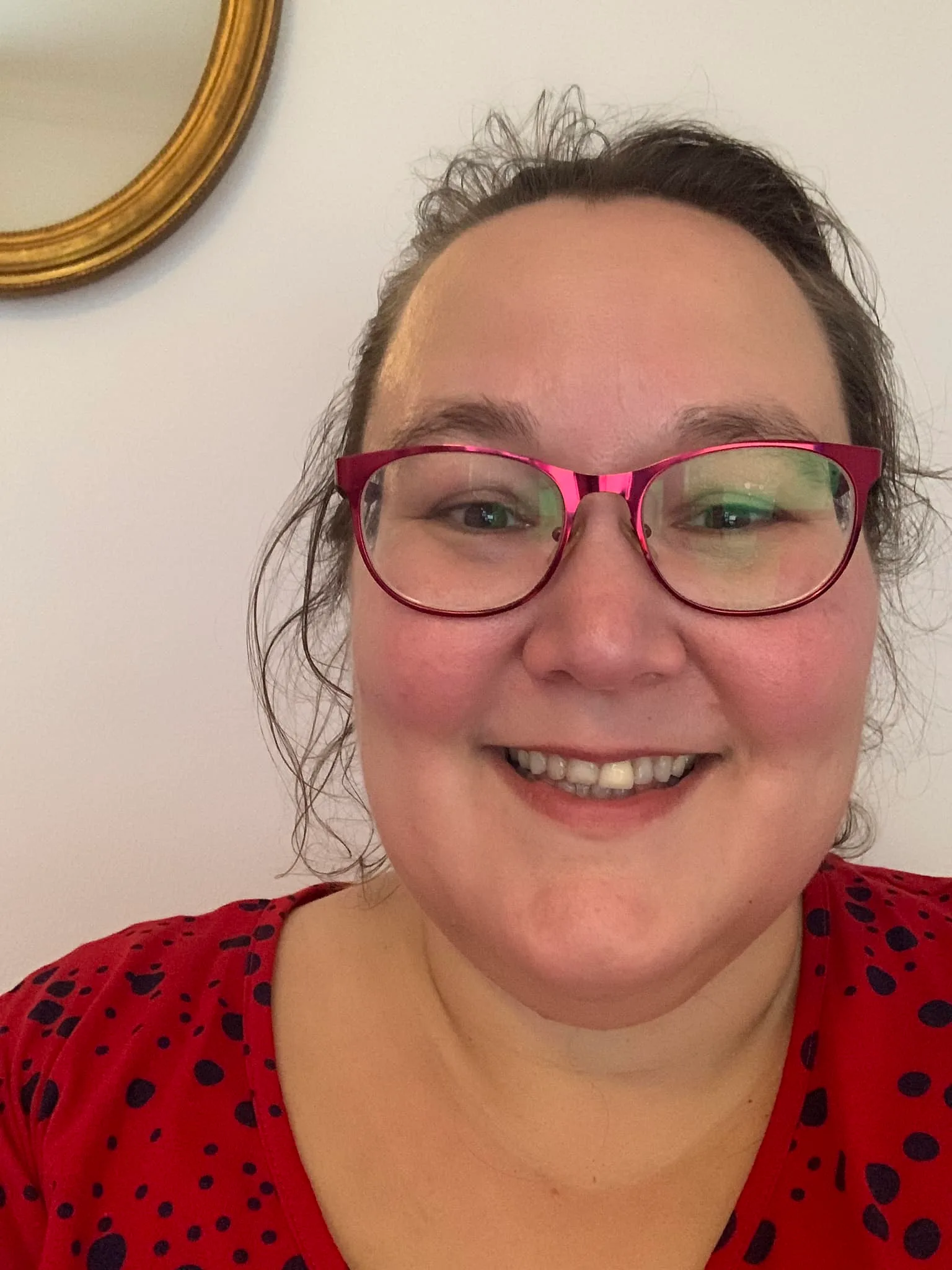 Frau mit Brille und roten Haaren in rotem Oberteil vor heller Wand, Nahaufnahme