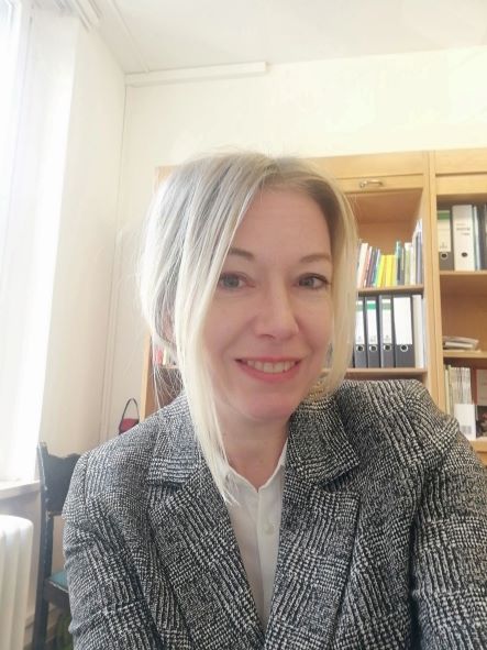 Frau mit langen glatten Haaren in grauem Blazer vor Bücherregal, Nahaufnahme