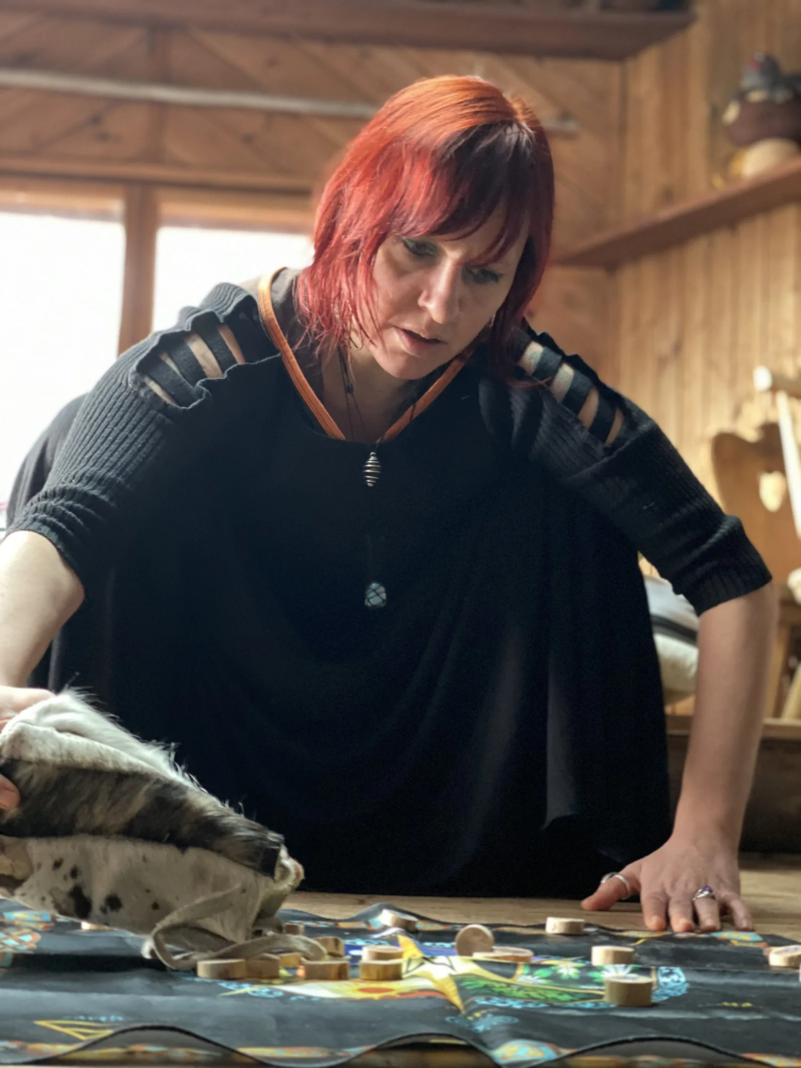 Frau mit roten Haaren arbeitet konzentriert mit Runenstabilen in Holzwerkstatt