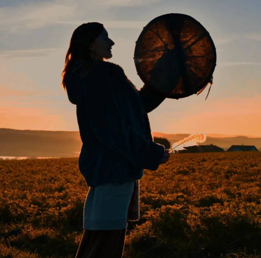 Sacred Woman Rising – Kurspaket heilige Weiblichkeit 39 Silhouette einer Frau vor Sonnenuntergang mit großem Tamburin und Feder gegen Landschaft