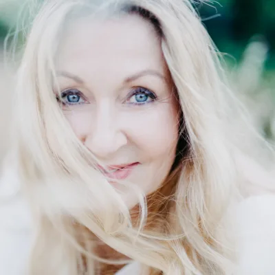 Sacred Woman Rising – Kurspaket heilige Weiblichkeit 13 Porträt von Julia Sobainsky mit hellblondem Haar und natürlichem Make-up vor grünem Hintergrund