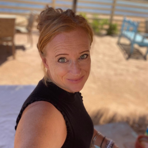Sacred Woman Rising – Kurspaket heilige Weiblichkeit 31 Elke Brenner mit rötlichem Haar am Strand in schwarzem Top