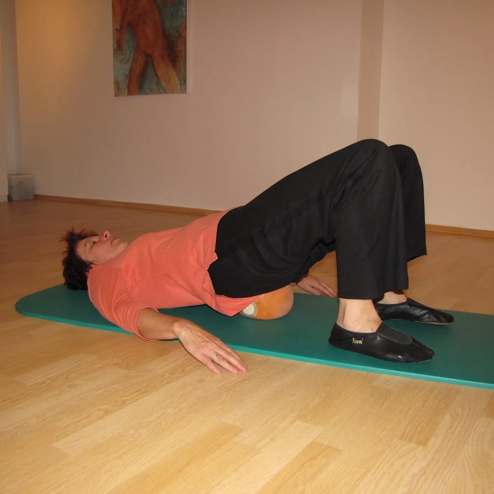 Frau in Sportkleidung auf Yogamatte in Brückenposition auf Holzboden
