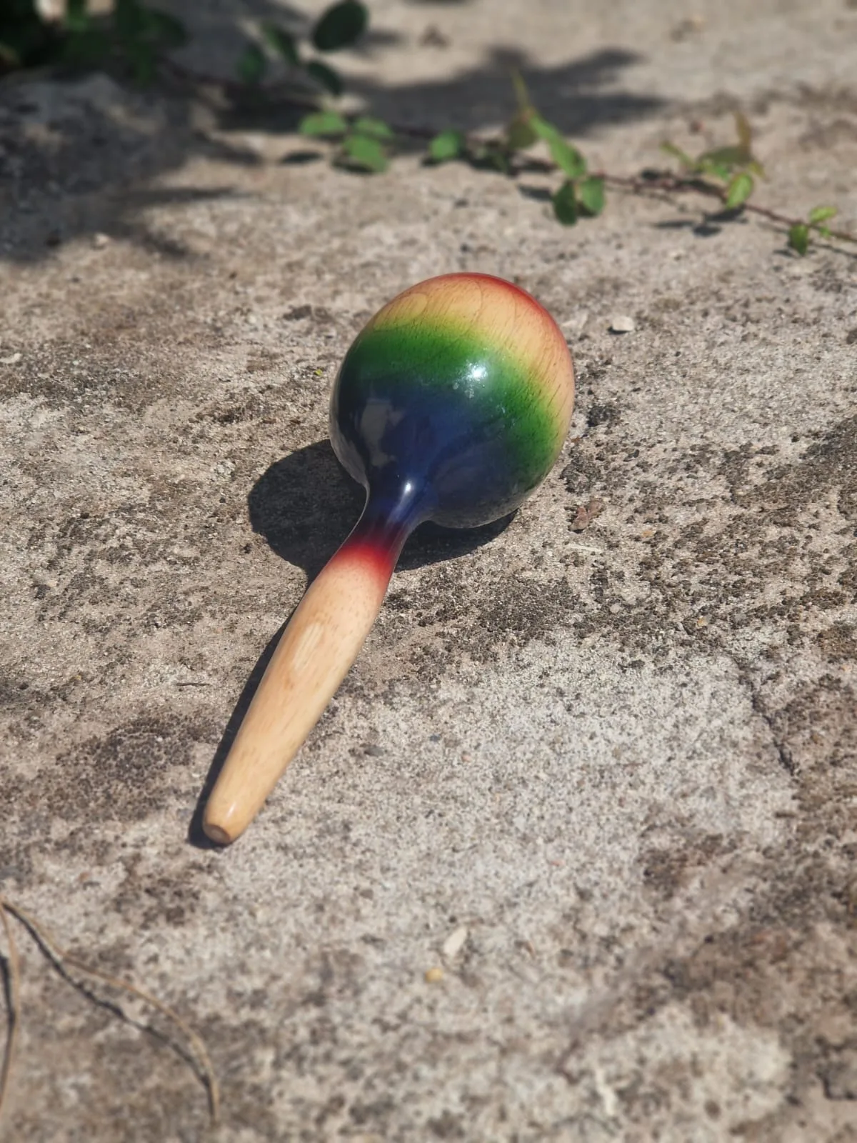 Regenbogenfarbiger Kristallstab mit Holzgriff auf sandigem Untergrund, spirituales Heilwerkzeug