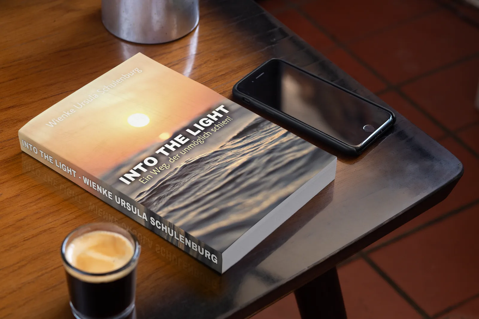Buchcover Into the Light mit Himmelsfotografie, neben Schwarzweiß-Porträt auf Holztisch mit Smartphone