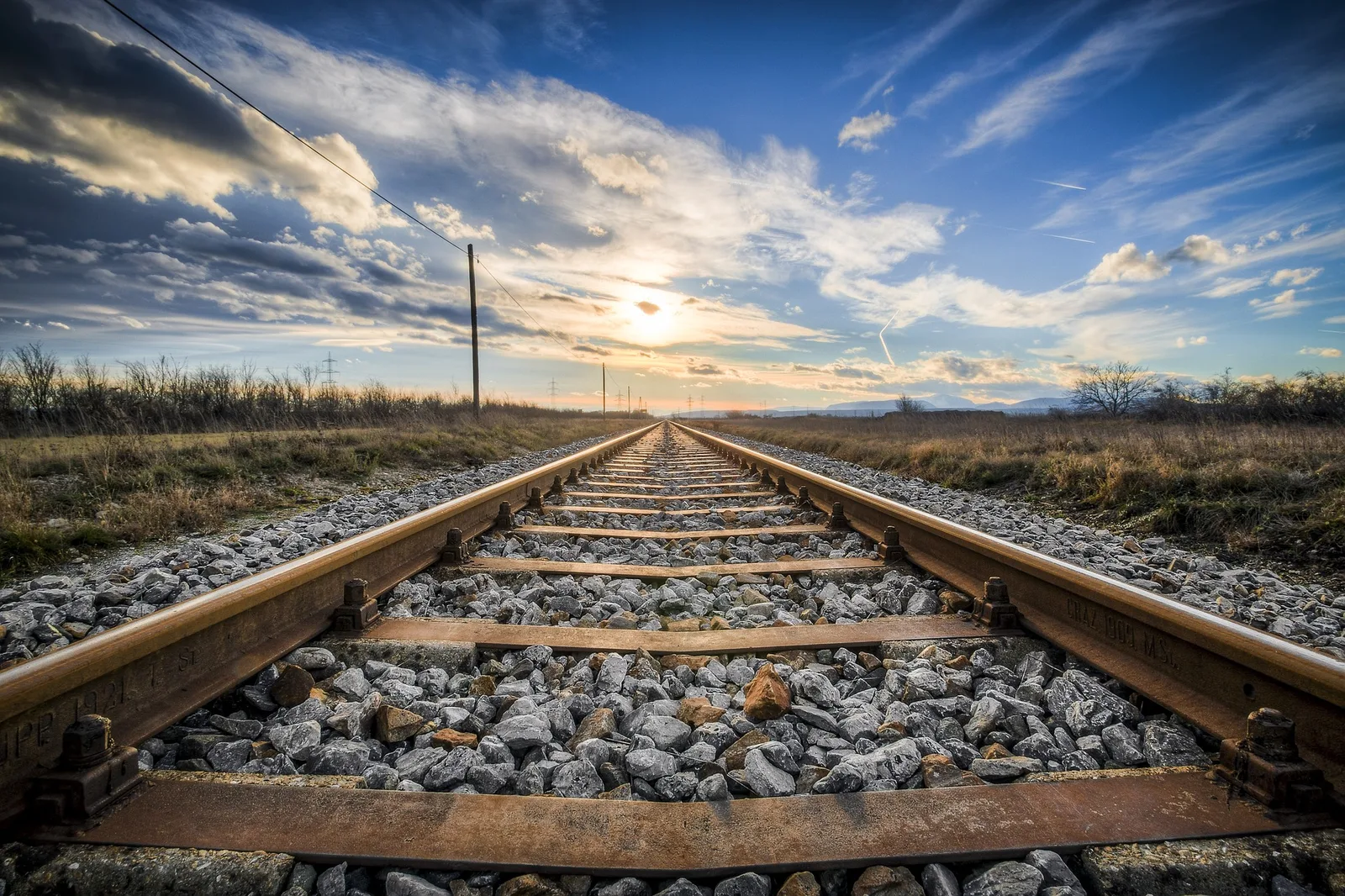 Eisenbahnschienen führen perspektivisch in Horizont, Landschaft mit Strommasten, dramatischer Himmel