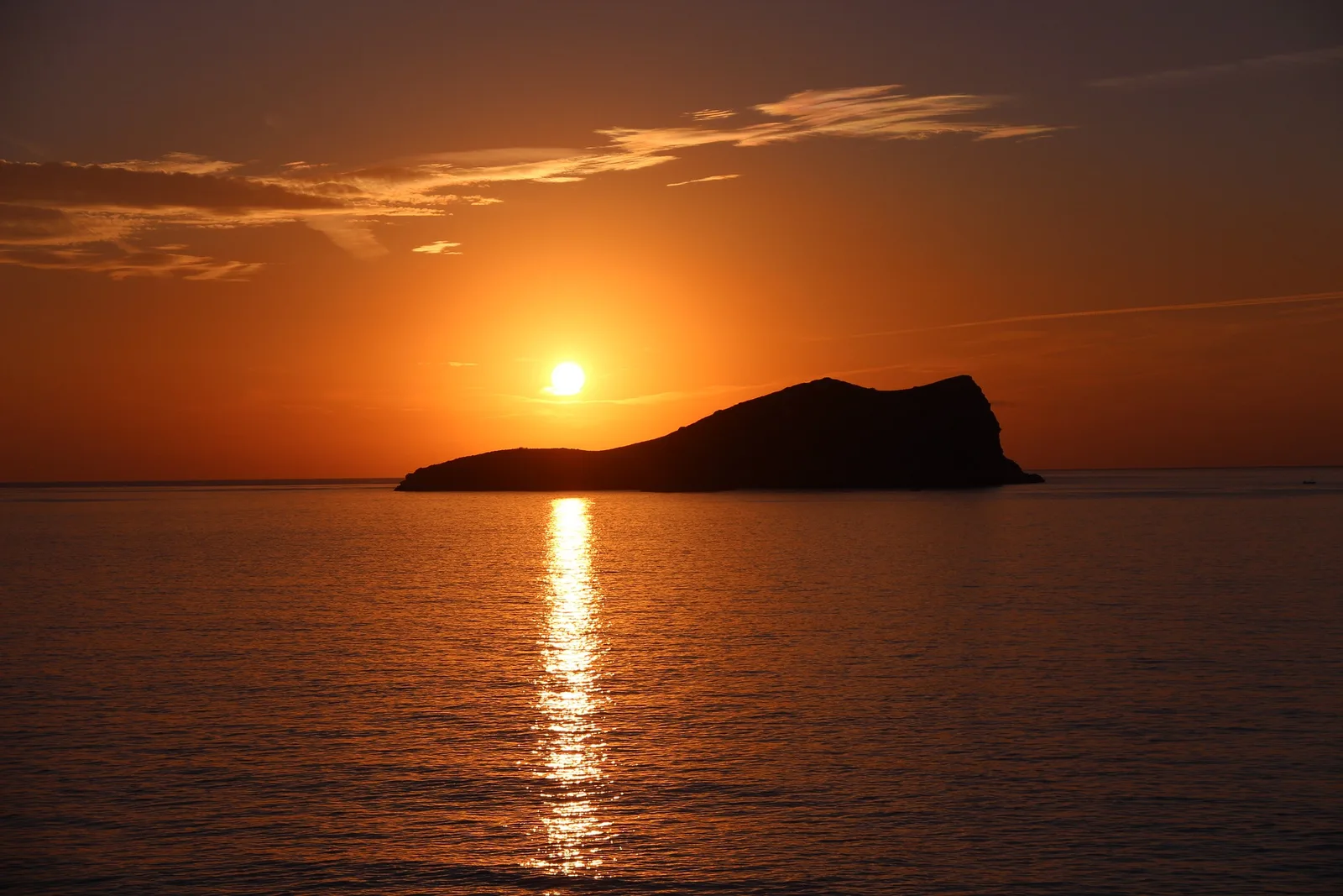 Sonnenuntergang über Mittelmeer mit Felsinsel im Gegenlicht, golden-orange Himmel spiegelt sich im Wasser