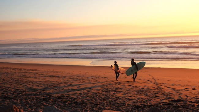 Zwei Surfer mit Boards am Strand bei Sonnenuntergang