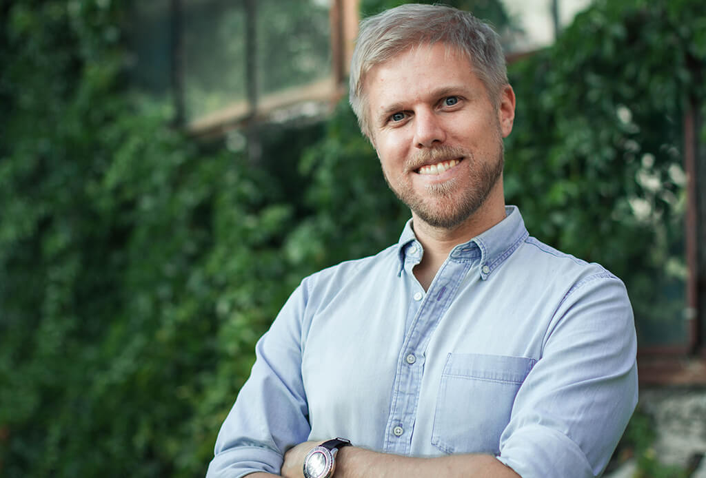 Porträt von Tim Hamer in hellblauem Hemd vor grüner Efeu-Wand
