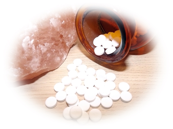 Produktabbildung Schüssler Salze mit weißen Tabletten in offener Glasflasche auf Holz