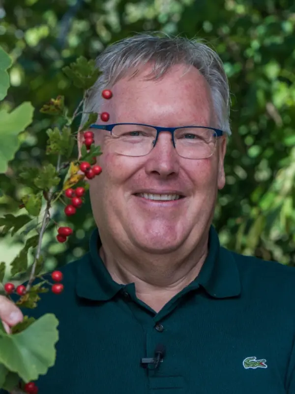 Porträt von Walter Käch mit Brille vor grünem Blätterhintergrund und Beeren