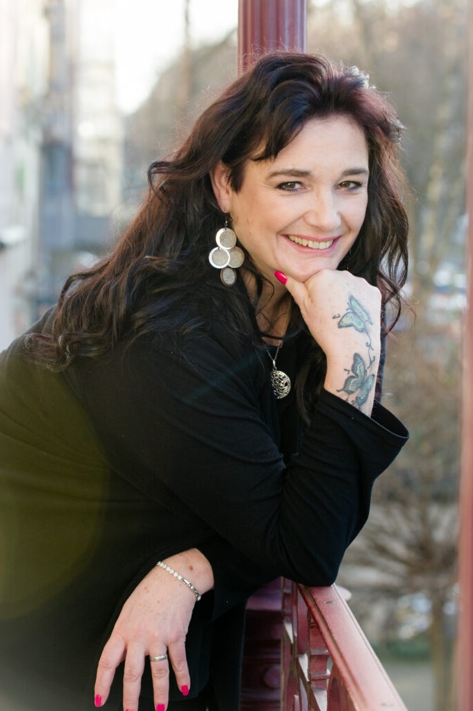 Professionelles Porträt Eva Maria Herzog mit Tattoos und Schmuck vor urbaner Kulisse