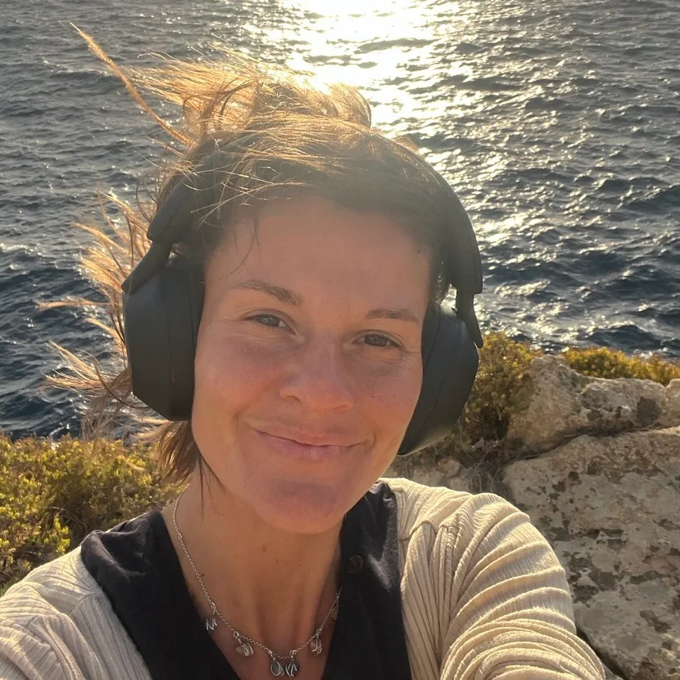 Frau mit Kopfhörern an Felsenküste mit Meereshintergrund und Sonnenlicht