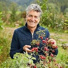 Frau mittleren Alters mit ergrauten Haaren hält Beeren-Strauch in grüner Natur