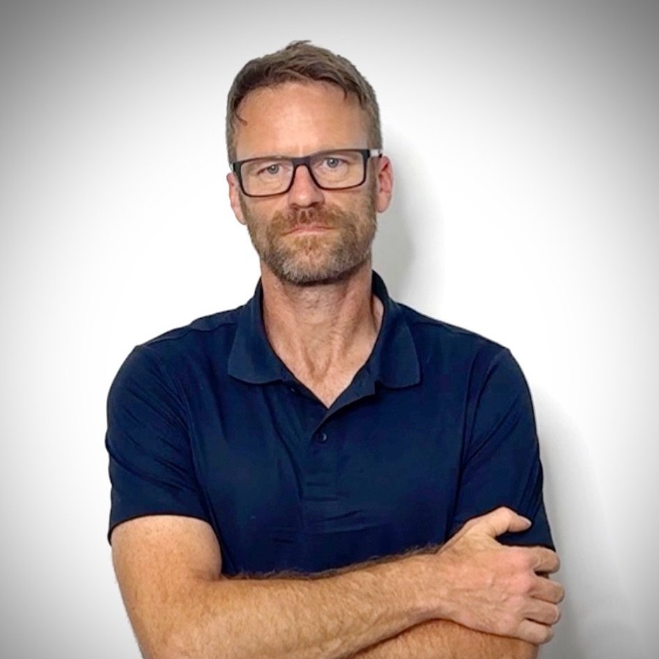 Portrait von Sebastian Krüger, Mann mit Brille in dunklem Poloshirt vor weißem Hintergrund