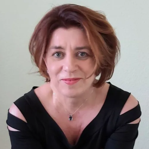 Ines Koban mit rotbraunem Haar und schwarzem Oberteil, Porträt vor hellem Hintergrund