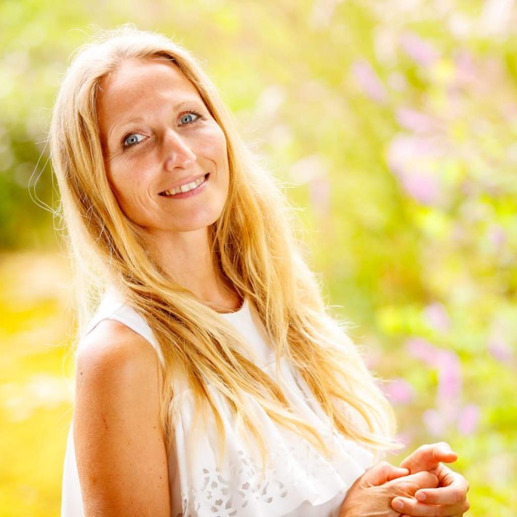 Frau mit rötlichem Haar und weißem Top vor Blumenwiese