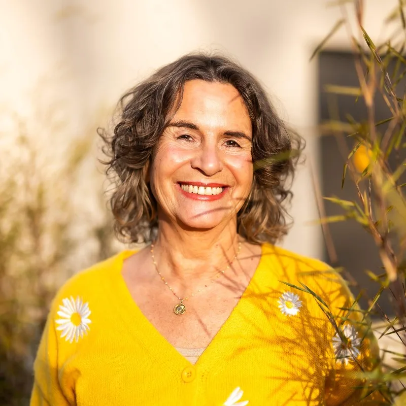 Porträt Bettina, Frau mit lockigen dunklen Haaren, gelbem Top mit Blumenmuster, Halskette, Sonnenlicht