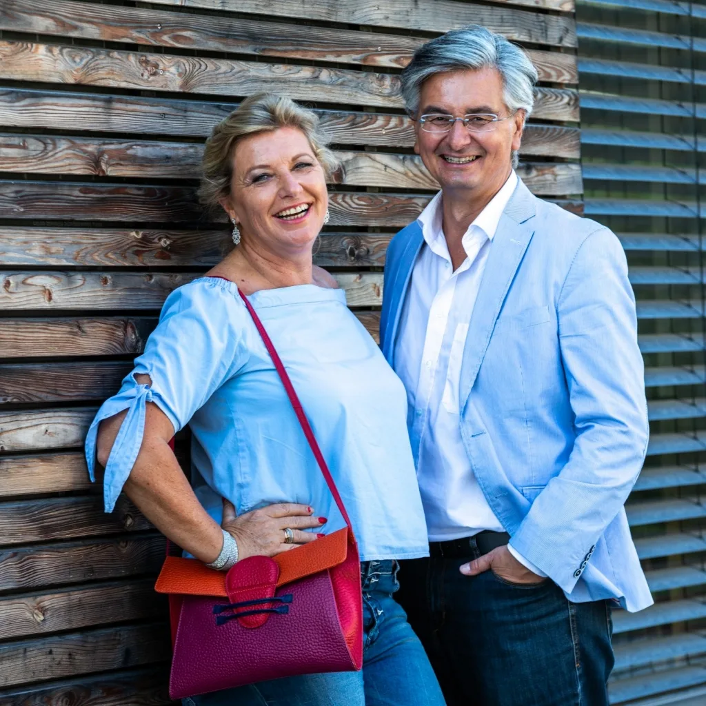 Porträt von Monika und Andreas Pott, elegantes Paar vor Holzwand, Frau in blauem Leinenoberteil, Mann in hellblauem Blazer