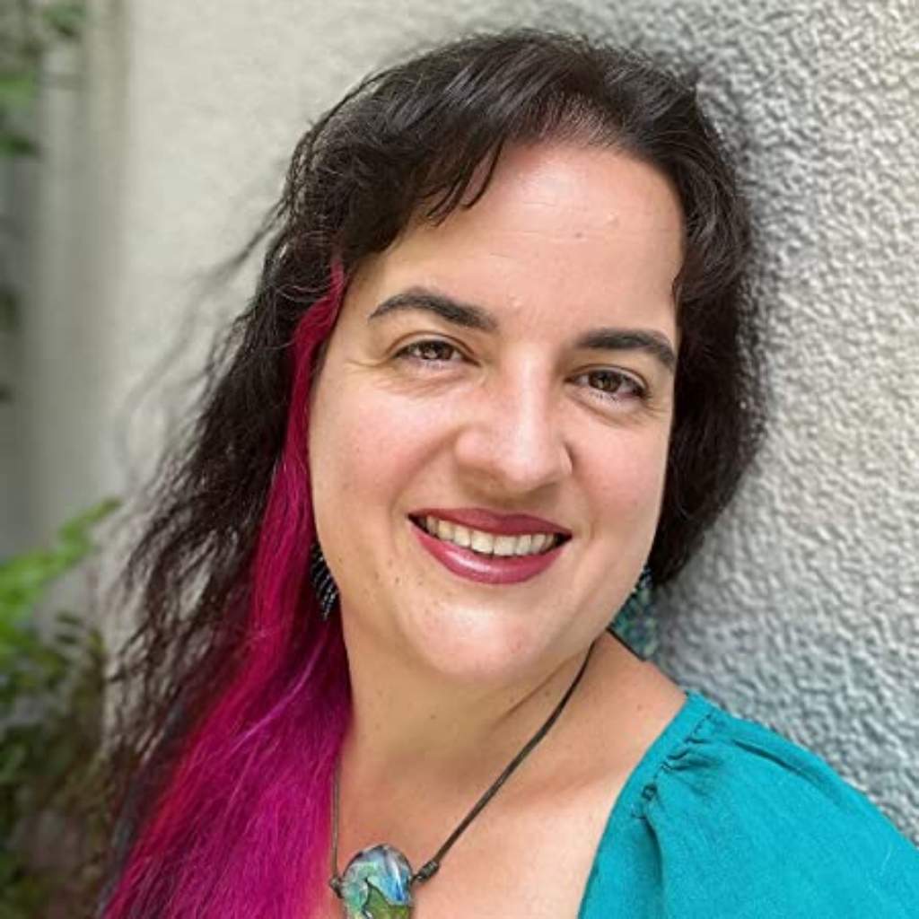 Porträt Marisa Schmid, Frau mit dunklen Haaren und pinkem Haarsträhnchen, türkisem Top, lächelnd vor grauer Wand