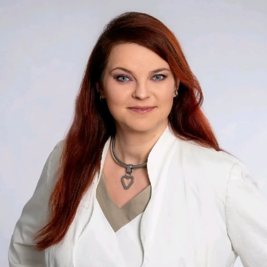 Porträt Bianca Sommer, Frau mit rötlichen Haaren, weißer Jacke, Herz-Halskette, grauer Hintergrund