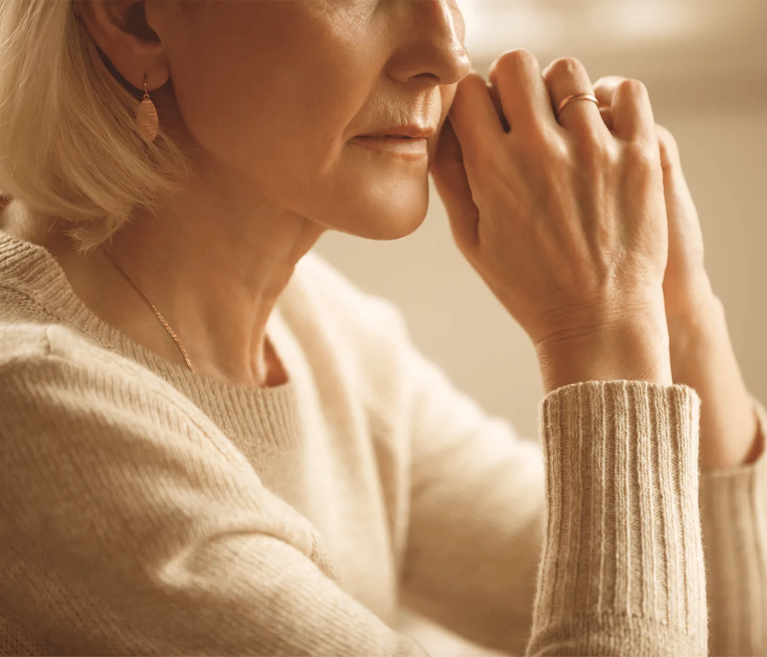 Nahaufnahme Frauengesicht mit Hand am Mund, helles Tageslicht, beige Pullover