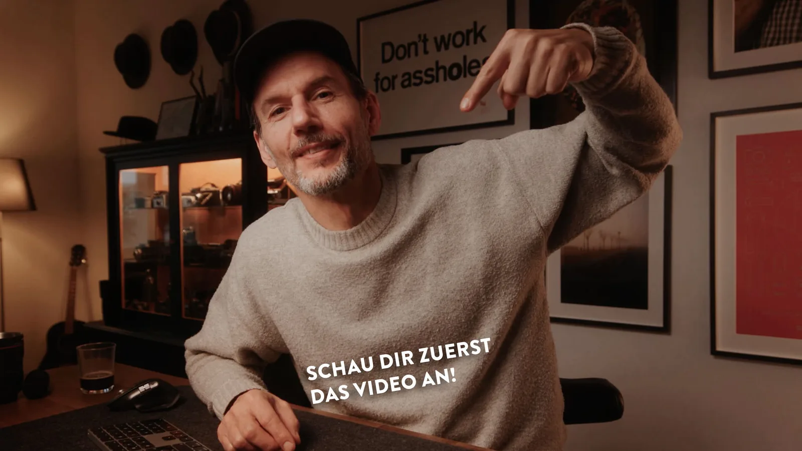 Autor Christian Anderl sitzt am Schreibtisch, zeigt auf Kamera, Text "Schau dir zuerst das Video an!"