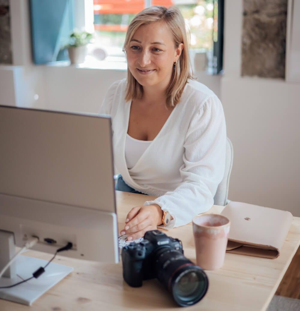Lisa Burth sitzt am Schreibtisch vor einem Laptop und einer professionellen Kamera