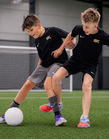 Zwei Jungen in schwarzem Trainingstrikot in Hallensportplatz trainieren mit Fussball