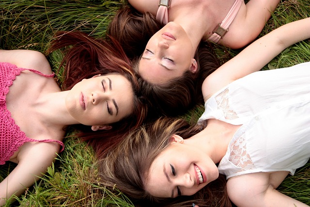 Drei Frauen liegen lachend nebeneinander auf grüner Wiese