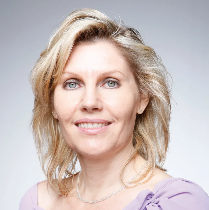 Porträt Frau mit blonden Haaren, lila Oberteil, lächelnd, hell grauer Hintergrund