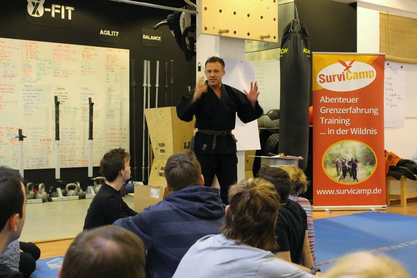 Selbstschutz & Verteidigung – Kurs zur Notwehr von Daniel Schäfer 2 Instructor unterrichtet Gruppe in Fitnessstudio mit SurviCamp-Banner