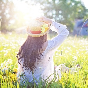 Mädchen auf sonniger Wiese mit Blumen trägt Strohhut und weißes Kleid