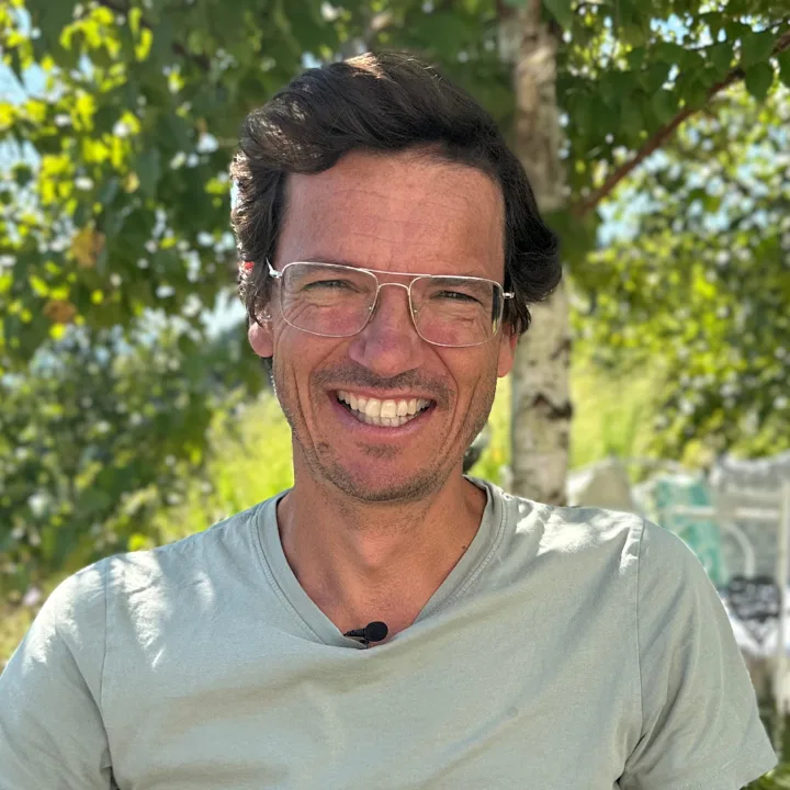 Markus Burkhard lächelt in die Kamera, hält Tomatenpflanze mit reifen Früchten