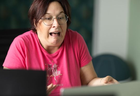 Marlen Kästner in Pink-Shirt lächelt vor Laptop-Bildschirm